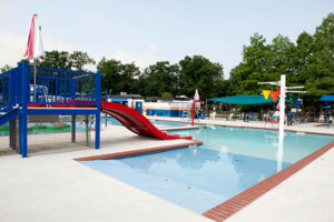 An outdoor pool with multiple play elements including a wide, red waterslide and green floating 