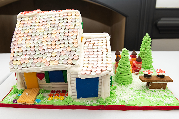 A gingerbread house with an attached garage. The building has white frosting siding, and a steep smartie-shingled roof. A sugar wafer walkway leads to the front door, and there's a starburst bouncy house in the side yard.