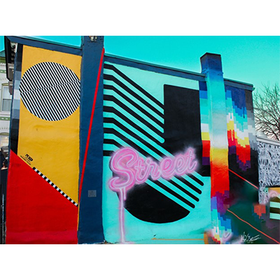 A colorful mural on the outside of a building, featuring bright colors, geometric shapes, and the cursive word 