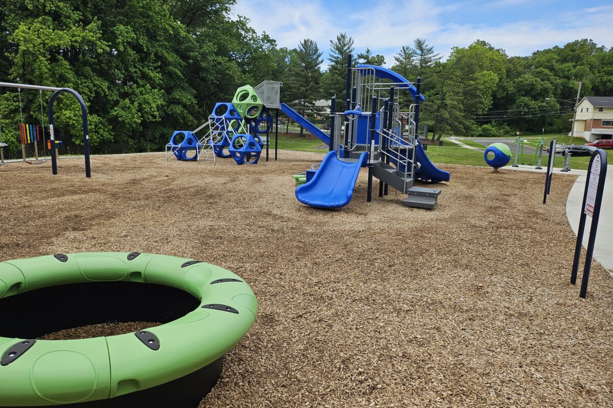 A blue and green outdoor playground with multiple play structures, featuring slides, platforms, stairs, climbing elements, spinning elements, swings, and more.