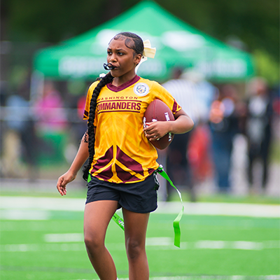 A woman holding a football and blowing a whistle on a football field