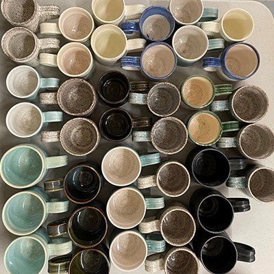 A collection of multi-colored ceramic mugs of various sizes and colors arranged in neat rows on a table.