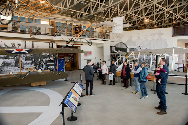 A group of visitors in an airplane museum surround by late model planes