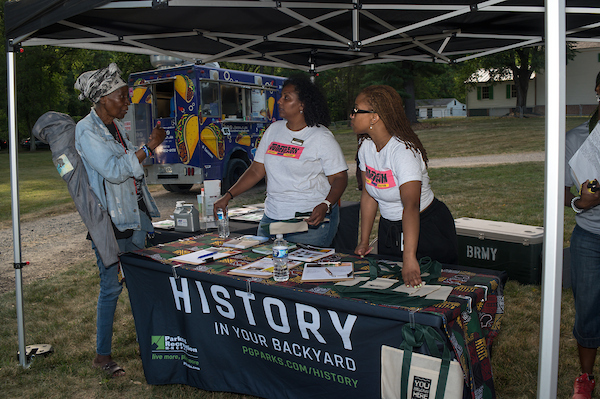 History in Your Backyard outreach table under a canopy, with staff sharing information at an outdoor community event.
