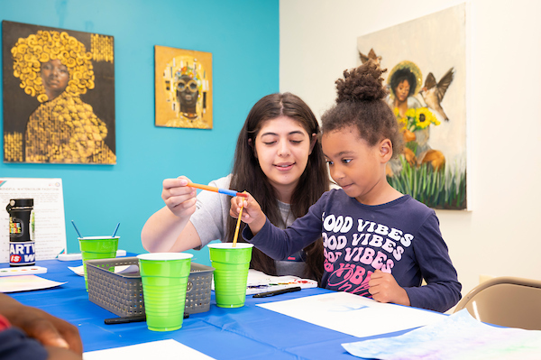 An adult assists a child with a watercolor painting project.