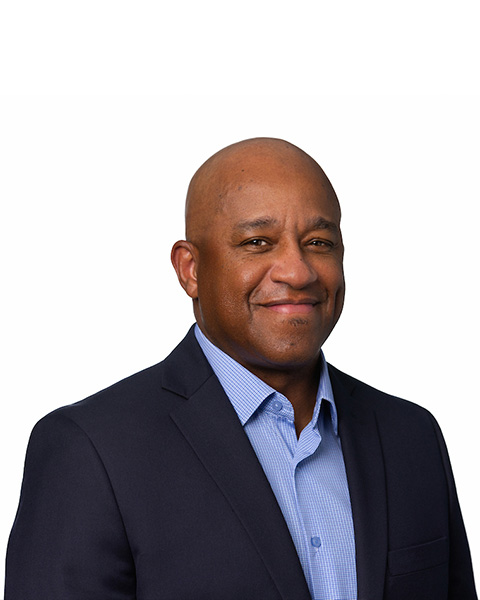Headshot of a smiling man wearing a dark jacket and a blue button-down shirt open at the collar.